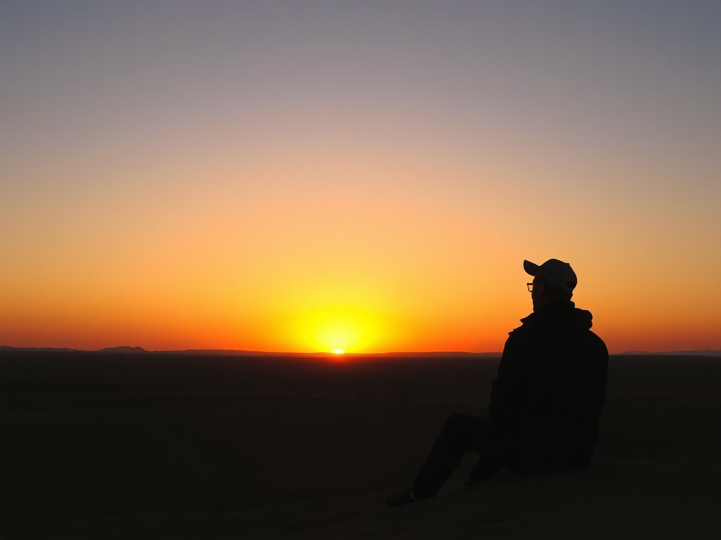 sunset over desert landscape with a traveler sitting quietly watching horizon, warm colors, stillness and reflection